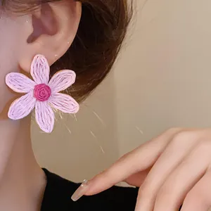 Detailed view of handmade pink woven flower stud earring with bohemian holiday style