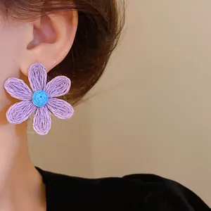 Close-up of bohemian purple and blue woven flower stud earring worn on model's ear