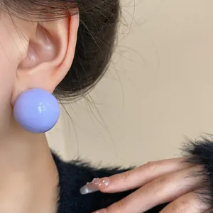 Dettaglio ravvicinato di un orecchino a sfera viola lucido indossato con eleganza sul lobo