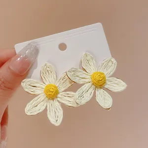 Close-up of Bohemian woven flower stud earrings with white petals and yellow center