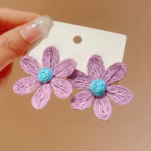 Detailed view of handmade purple woven flower stud earrings with bohemian vacation style.