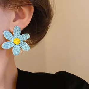 Close-up detail of a handmade blue woven flower earring with a yellow center in bohemian style