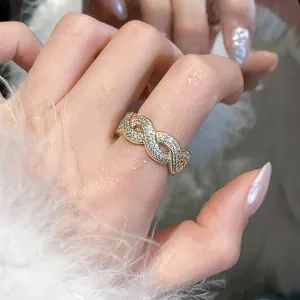 Dettaglio di un anello intrecciato in oro con zirconi brillanti indossato al dito