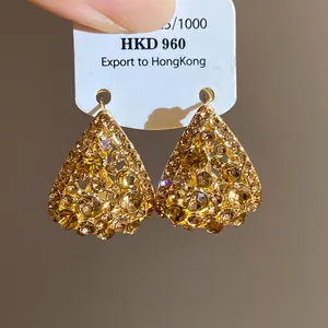 Dettaglio di orecchini a goccia traforati con strass scintillanti in finitura oro vintage.