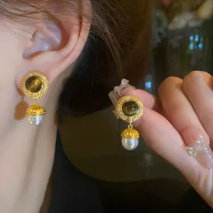 Dettaglio orecchini vintage in oro con pietra occhio di tigre e perla bianca