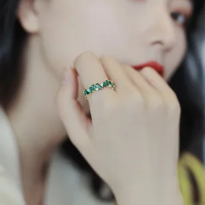 Close-up detail of a vintage gold-plated ring with emerald green zircons on a finger