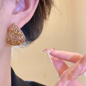 Primo piano di eleganti orecchini a goccia dorati traforati con cristalli indossati.