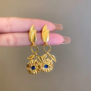 Dettaglio ravvicinato di orecchini floreali in oro stile vintage con gemme blu centrali