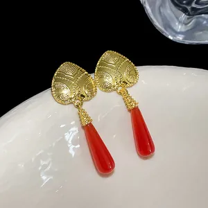 Dettaglio di orecchini vintage a cuore in oro con ciondolo a goccia rosso su piatto bianco