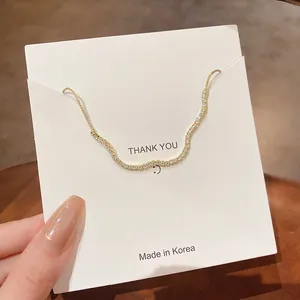 Detail eines minimalistischen Goldarmbands mit Kristallen auf einer weißen Dankeskarte