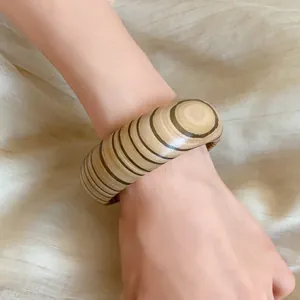 Macro view of a retro wood grain wide bangle worn on the wrist against beige fabric