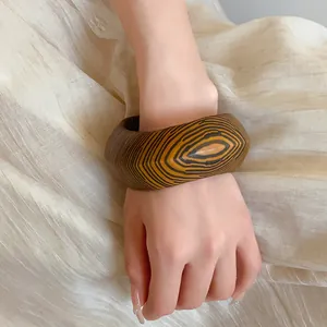 Close-up of a vintage chunky wooden-pattern bangle worn on a wrist over textured fabric