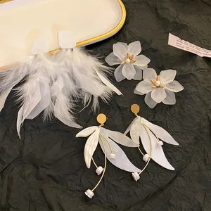 Close-up of white flower and feather drop earrings with gold accents on black background.