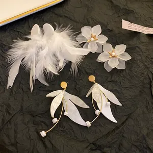 Collection of elegant white feather and floral tassel earrings on textured background