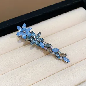 Elegant blue crystal floral hair clip presented on a textured jewelry display tray.