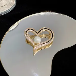 Detailansicht einer herzförmigen Brosche mit glitzernden Zirkonen und einer weißen Perle