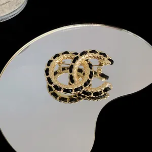 Detailansicht einer gold-schwarzen Brosche mit verschlungenem CC-Logo auf einer Spiegelfläche.