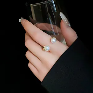 Elegant pearl open ring with gold pleated edges shown on finger holding a glass