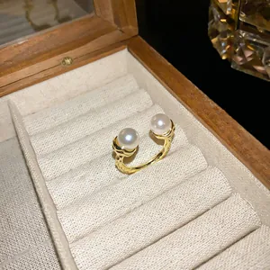 Macro view of a gold pleated open ring featuring two white pearls in a jewelry box