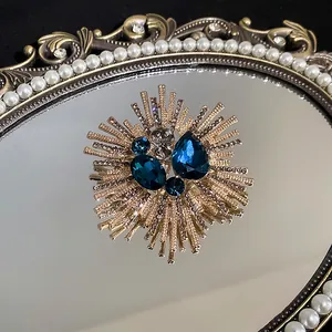 Detailansicht einer vergoldeten Sonnenstrahl-Brosche mit blauem Zirkon auf einem Perlenspiegel.