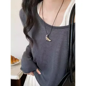 Dettaglio di una collana con ciondolo a croissant minimalista e cordino nero su maglia
