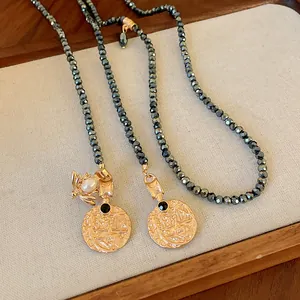 Close-up of vintage gold coin necklace with bee charm and metallic grey beads