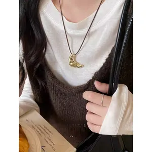 Dettaglio della collana con ciondolo a croissant su cordoncino nero sopra camicia bianca
