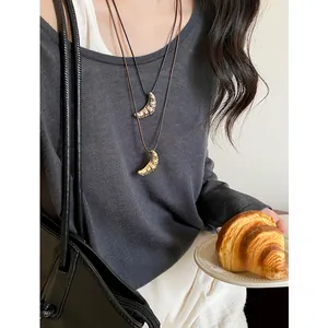 Dettaglio di collane con ciondolo a croissant minimaliste su cordini neri con maglione grigio