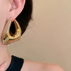 Close-up detail of chunky gold-plated irregular geometric hoop earrings on a model's ear