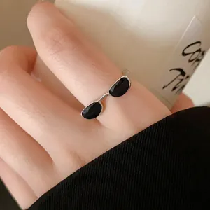 Close-up detail of a creative sunglasses-shaped open ring with black enamel lenses on a finger.