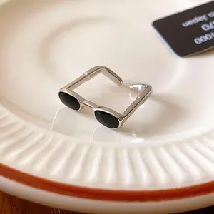 Close-up view of a unique silver sunglasses shaped open ring featuring black enamel lenses