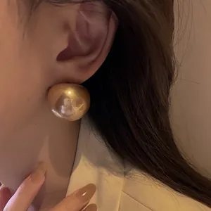 Primo piano di una modella che indossa un grande orecchino retrò dorato a forma di fagiolo