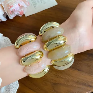 Detail view of vintage acrylic marbled oval link bracelets in gold and pink on wrist.