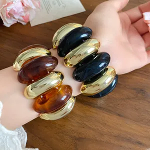 Detailed macro view of oversized retro acrylic spliced bracelets in gold and resin tones