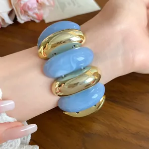 Detailed view of chunky acrylic swirled and gold oval link bracelet on wrist.