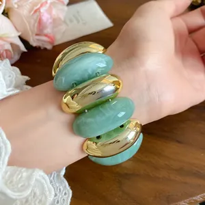 Close-up view of a green marbled acrylic and gold-tone metal chunky bracelet on a wrist