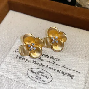 Close-up detail of French vintage matte gold flower stud earrings with sparkling zircon centers