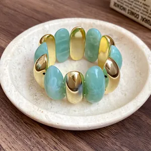 Close-up view of chunky green marble and gold-tone oval bead stretch bracelet on a dish