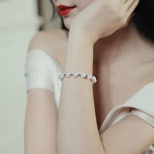Detail view of a minimalist white pearl bracelet with gold beads on a model's wrist.