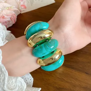 Close-up of turquoise swirl acrylic and gold oval bead bracelet worn on the wrist