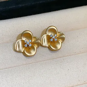 Detailed macro view of elegant matte gold flower stud earrings with zircon crystals