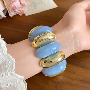 Close-up of blue marbled and gold oval acrylic bracelet worn on a female wrist