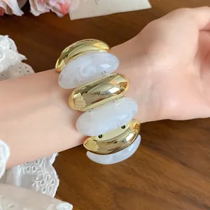 Detailed shot of white marbled acrylic and gold oval link bracelet on wrist
