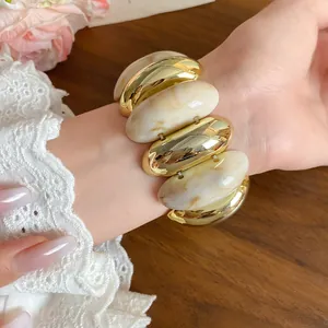Detailed view of an exaggerated marbled acrylic and gold metallic oval bead bracelet worn on wrist.