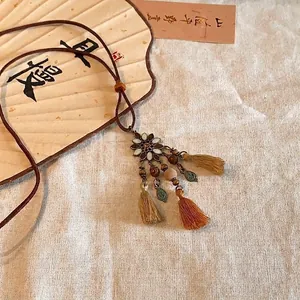 Detail showing ethnic flower pendant with wooden beads and tassels on fabric background.