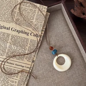Vintage ethnic style necklace with cream round pendant and blue beads on retro paper