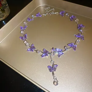 Makrodetail einer funkelnden lila Glas-Schmetterlingskette auf goldenem Tablett