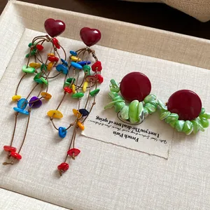Close-up detail of vintage dark red heart shell tassel earrings and green shell stud set