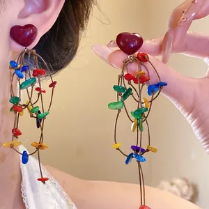 Close-up of vibrant heart stud earrings with colorful shell tassel charms