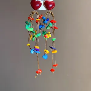Detailed view of red heart earrings with vibrant rainbow shell tassels on brown cords